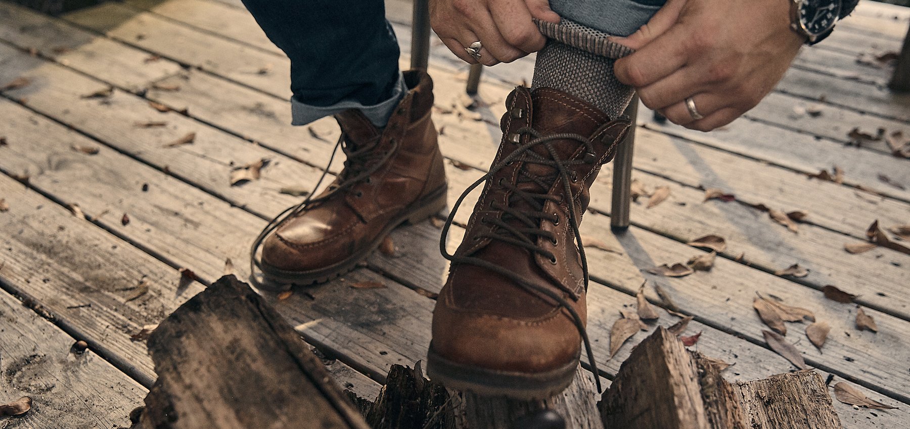 man putting on boots on wood deck